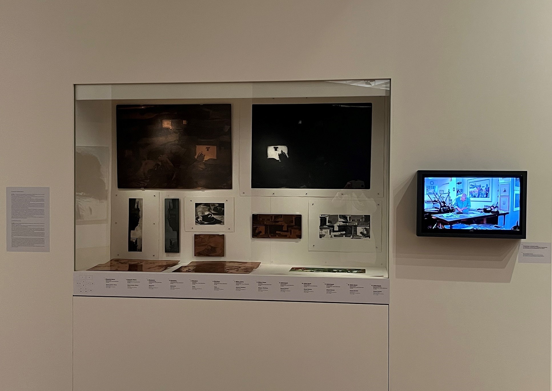 Display case with printmaking plates and prints. On the screen to the right, a video of Tetsis in his studio. Highlight from the exhibition