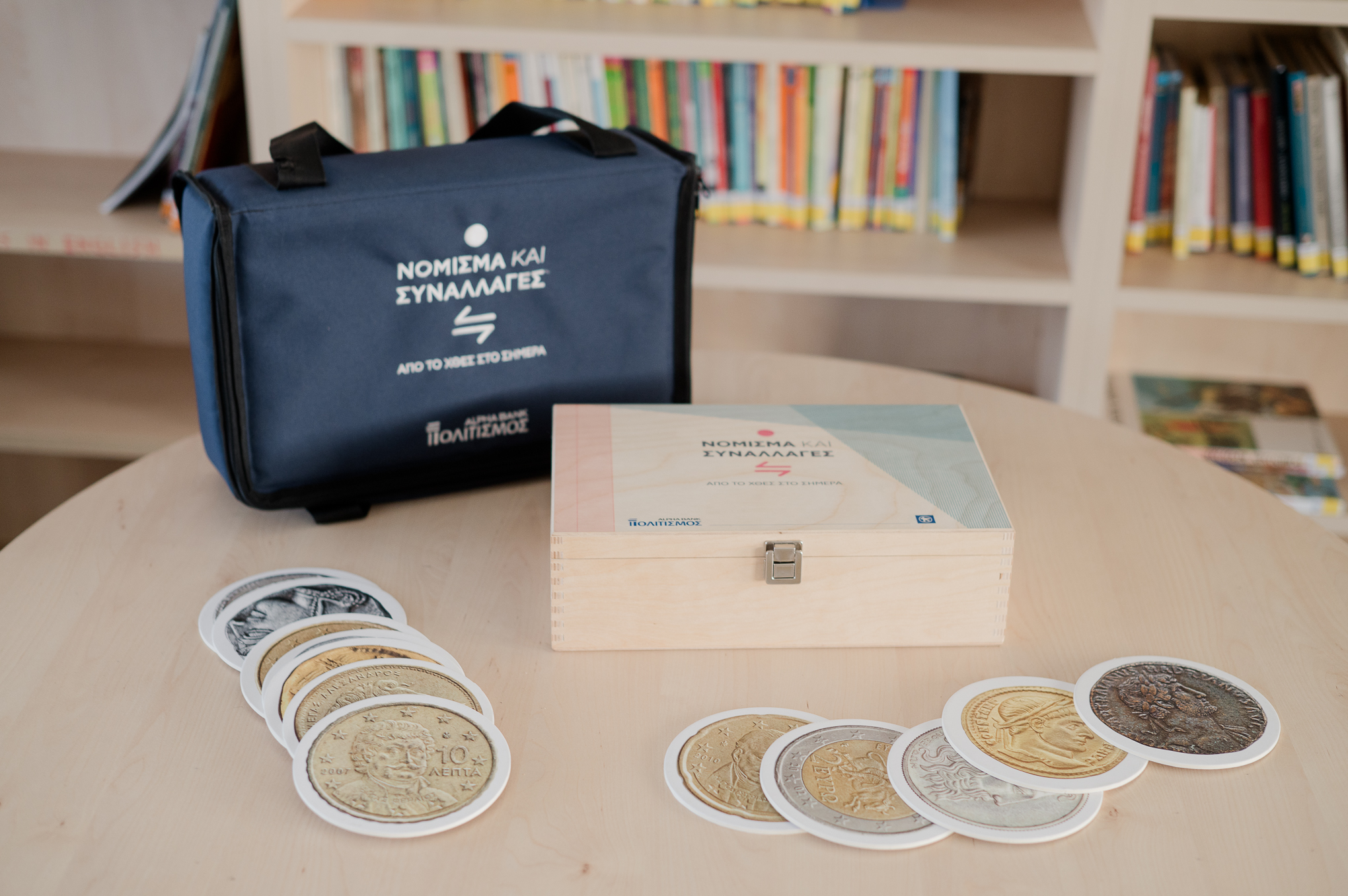 Blue suitcase, wooden case and paper coin replicas on a wooden table. Currency and Transactions Travelling Museum Case