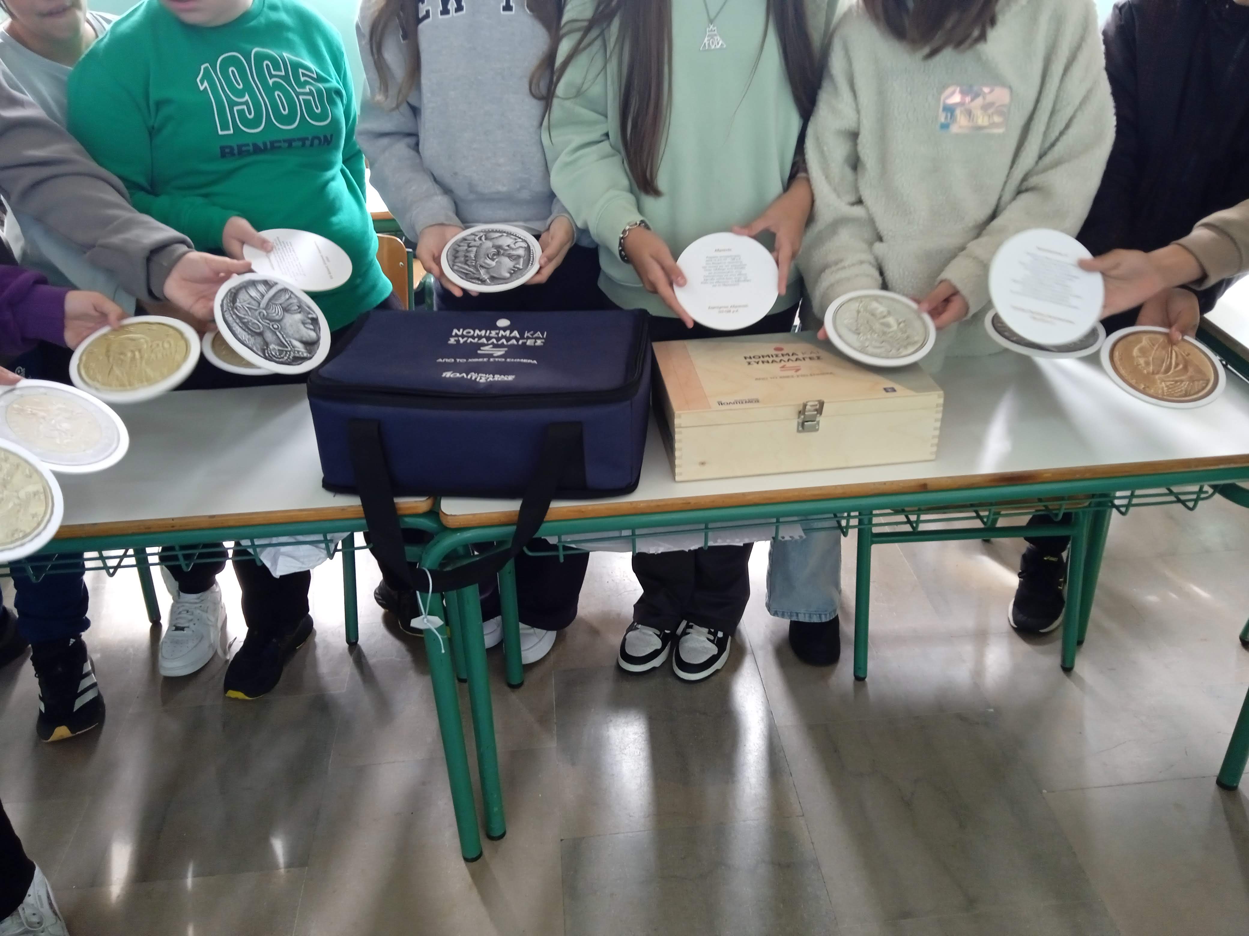 Children holding coin cards. In front of them, the “Currency and Transactions” museum kit. Children with coin cards