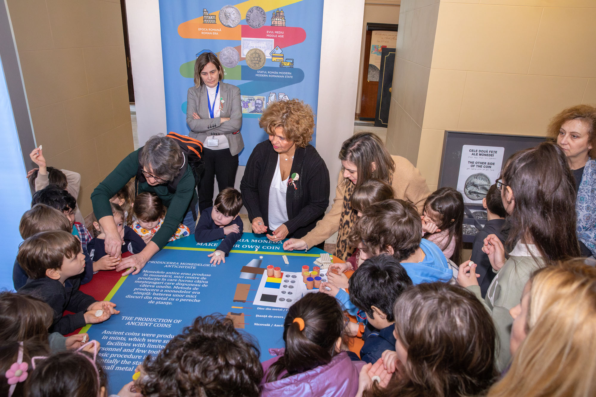 Τα παιδιά σε κύκλο φτιάχνουν νομίσματα από πλαστελίνη υπό την καθοδήγηση της κυρίας Δήμητρας Τσαγκάρη. Στιγμιότυπο από τη δημιουργική δραστηριότητα