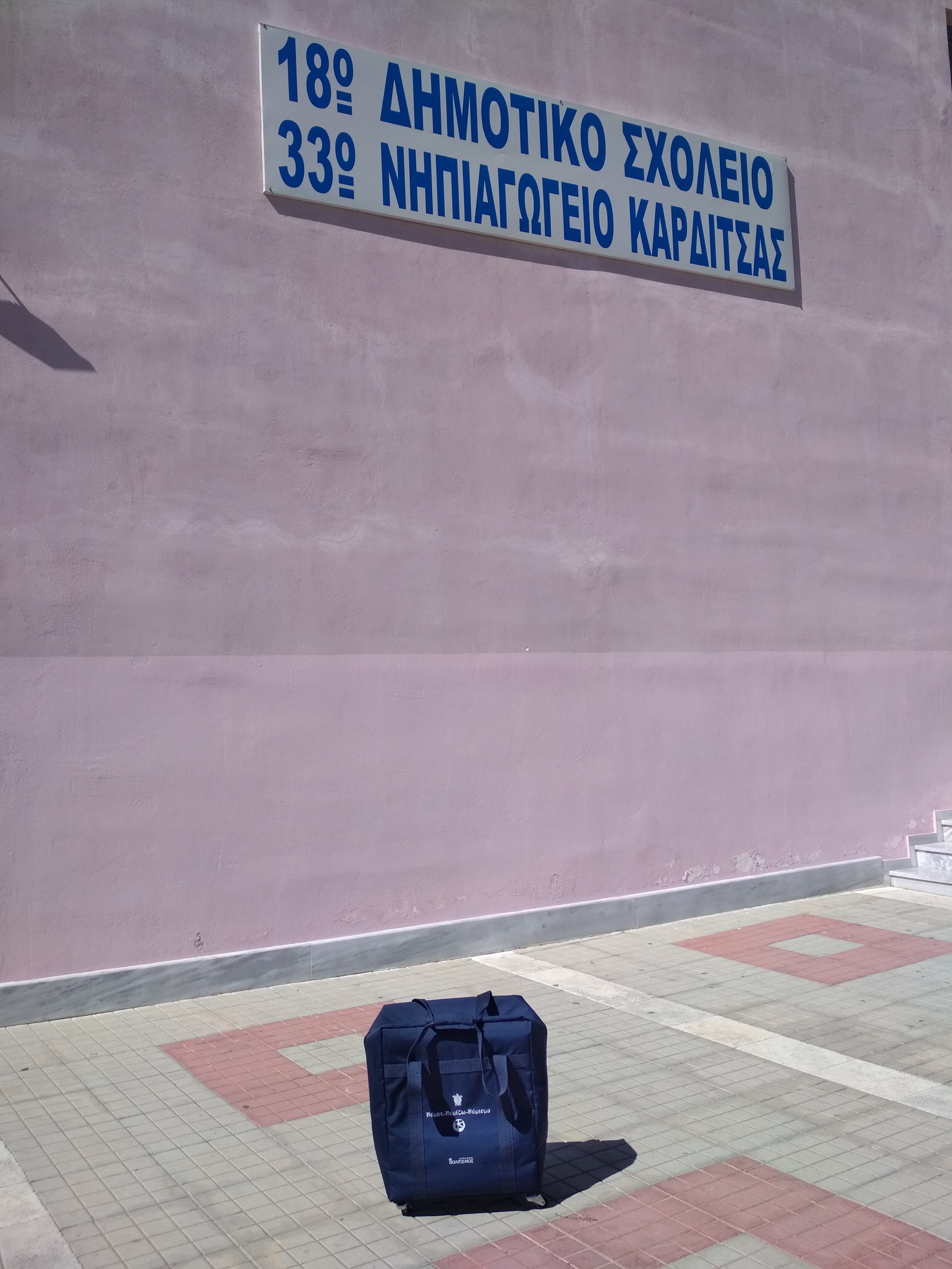 Η μουσειοβαλίτσα τοποθετημένη κάτω από την επιγραφή του 18ου Δημοτικού Καρδίτσας.  18ο Δημοτικό Καρδίτσας