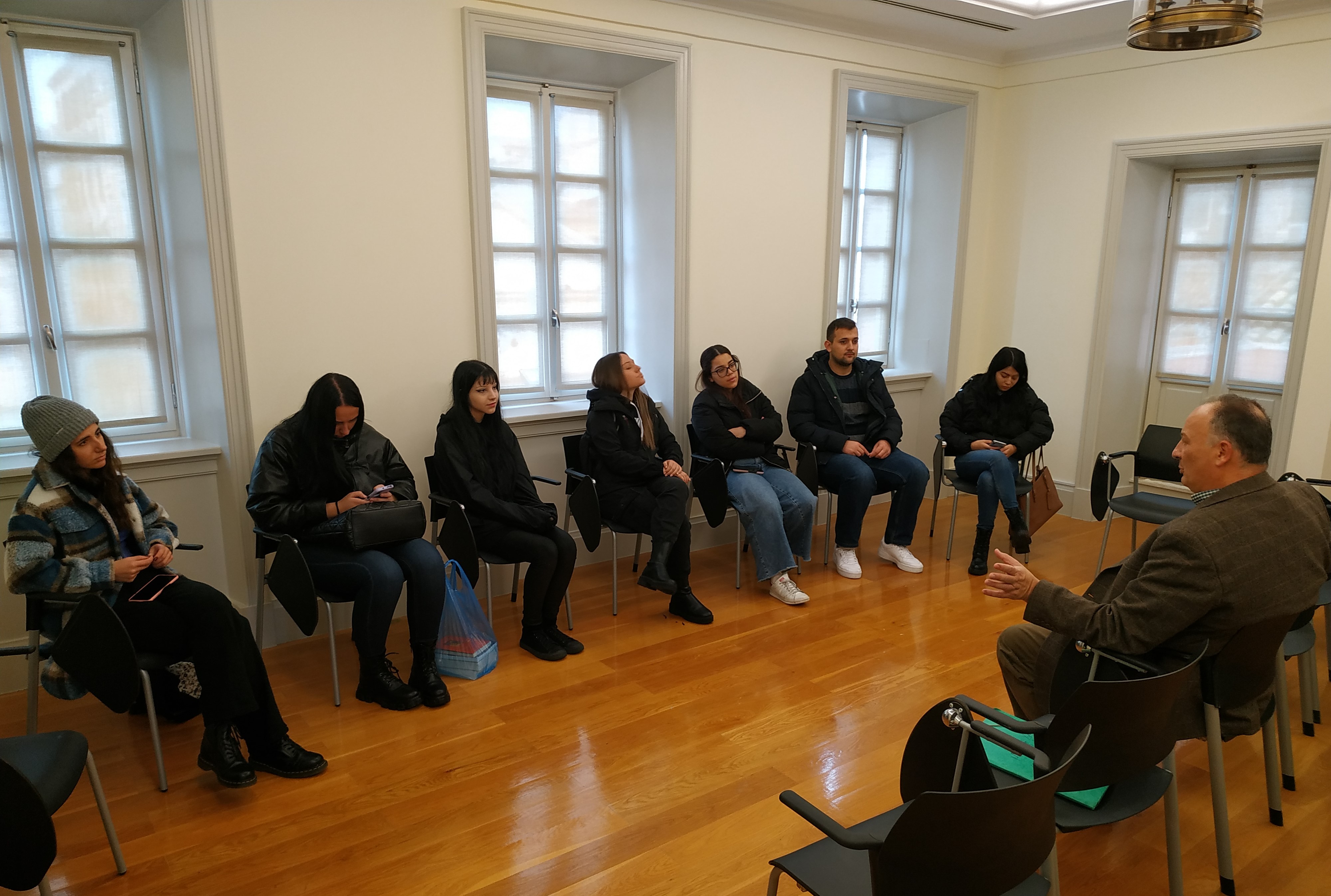 Professor delivering a lecture to students. They are seated in a circle in a museum hall.  The Banknote Museum of Ionian Bank on Corfu partners with the Ionian University