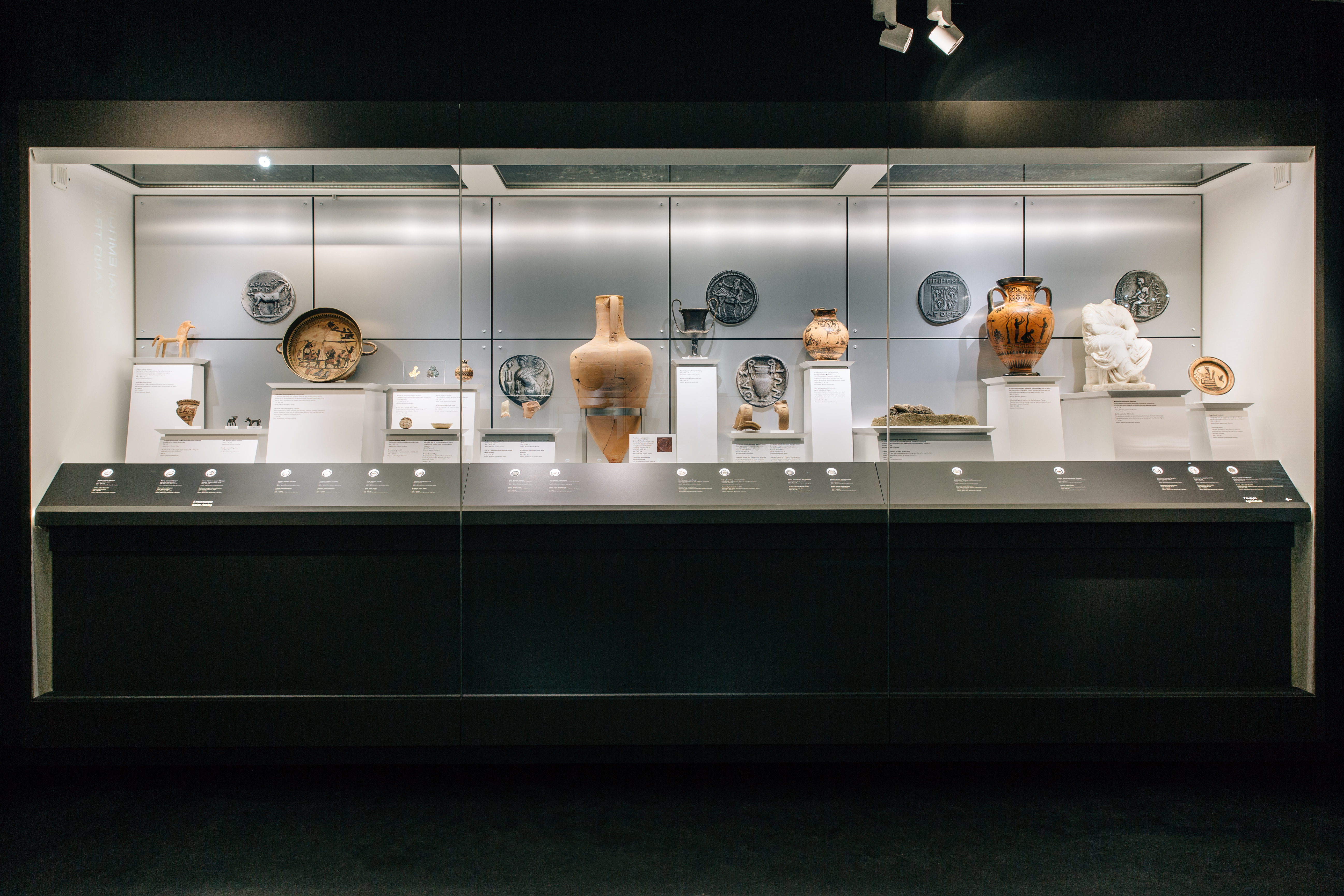 The exhibition area with exhibits in illuminated cases.  Exhibits “Money. Tangible Symbols in Ancient Greece”