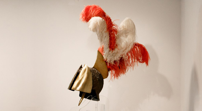 Μπρούντζινη περικεφαλαία με φτερά, μπροστά από λευκό τοίχο πάνω σε διάφανη βάση.  Μπρούντζινη περικεφαλαία με φτερά, μπροστά από λευκό τοίχο πάνω σε διάφανη βάση.