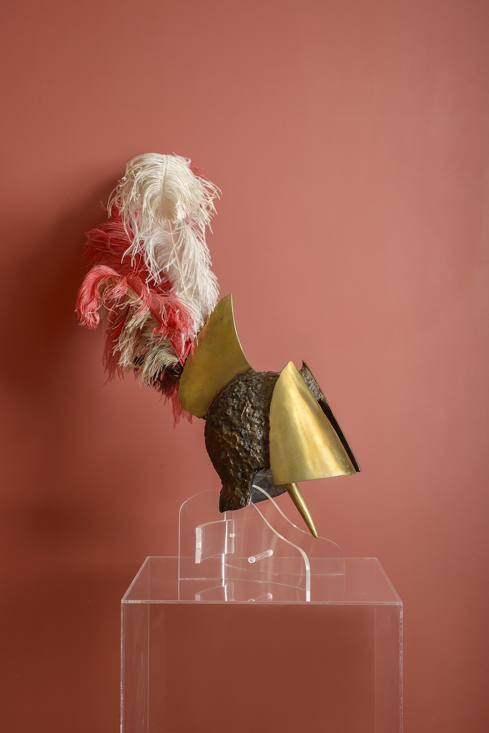 Μπρούντζινη περικεφαλαία με φτερά, μπροστά από κόκκινο τοίχο πάνω σε διάφανη βάση.  Μπρούντζινη περικεφαλαία με φτερά, μπροστά από κόκκινο τοίχο πάνω σε διάφανη βάση.